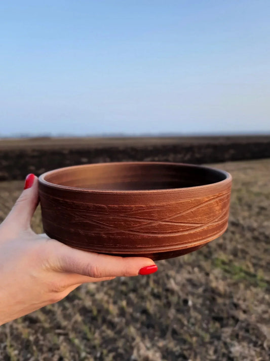 Hand holding a rustic handmade clay bowl outdoors, artisan earthenware from clayproductsshop