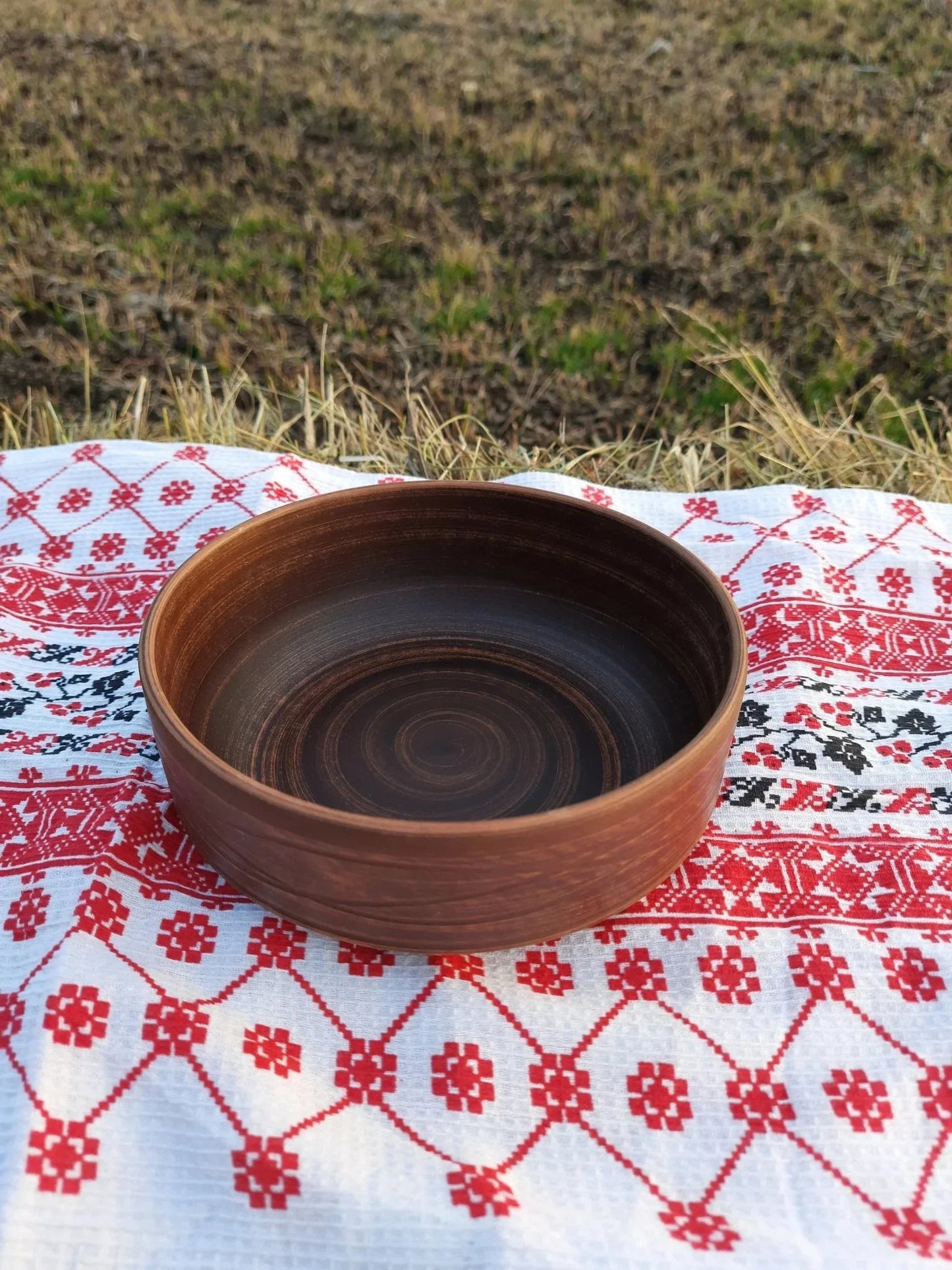 Handmade clay bowl with rustic finish on a patterned cloth, artisan earthenware homeware
