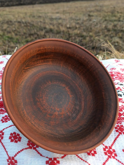 Handmade red clay bowl on patterned cloth, artisan pottery homeware outdoors