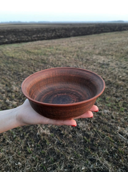 Hand holding handmade red clay bowl outdoors, artisan pottery homeware from clayproductsshop