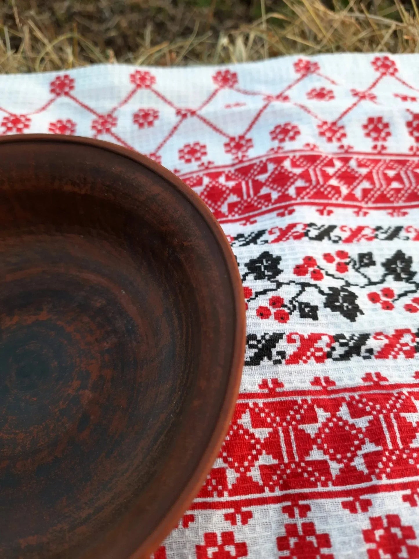 Handmade brown clay bowl on embroidered red and white cloth, artisan pottery homeware
