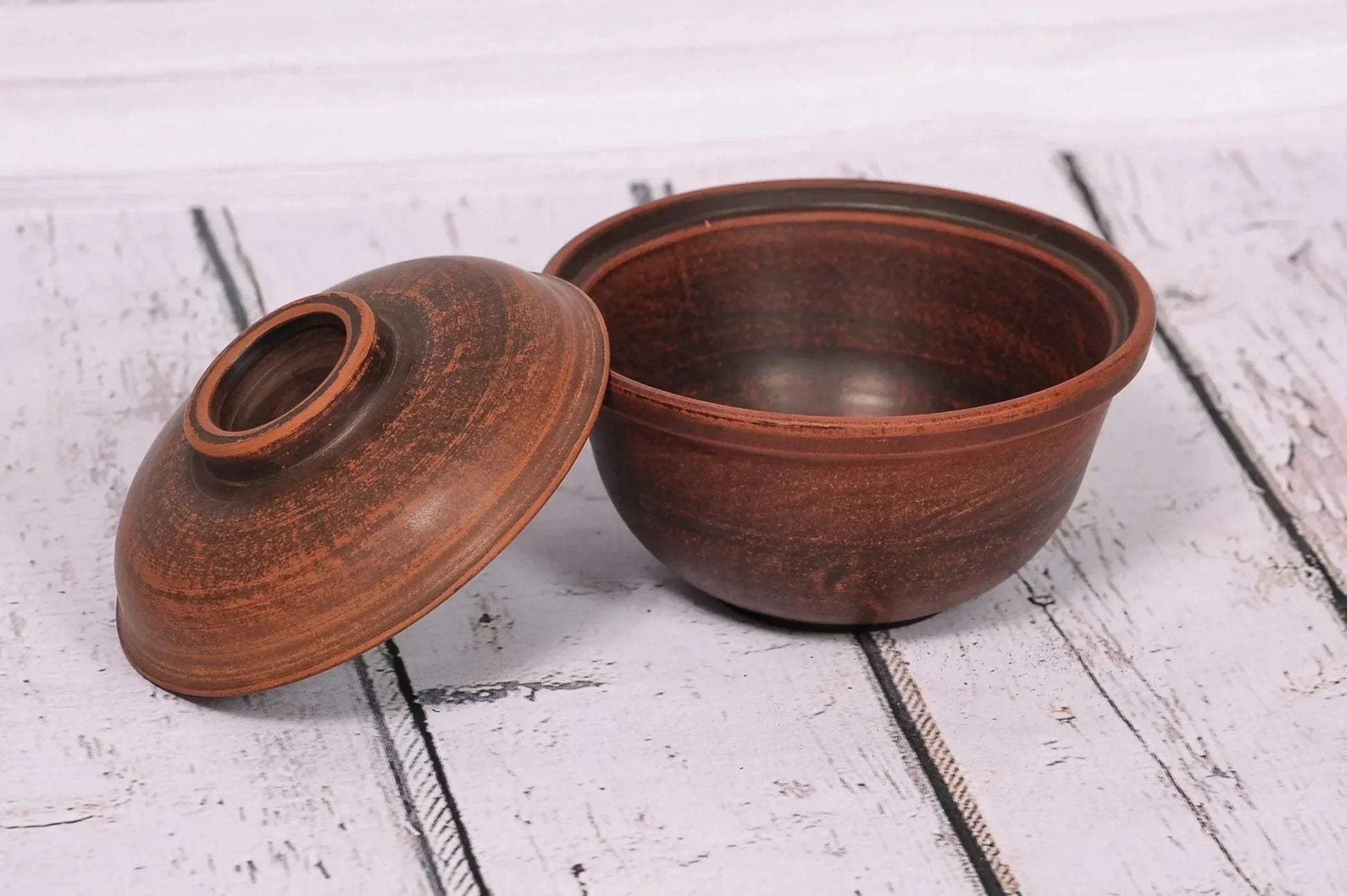 Handmade clay bowl with lid on rustic wood surface, artisan pottery kitchenware