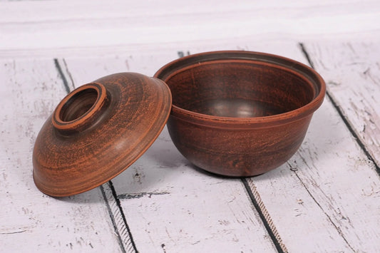 Handmade clay bowl with lid on rustic wood surface, artisan pottery kitchenware