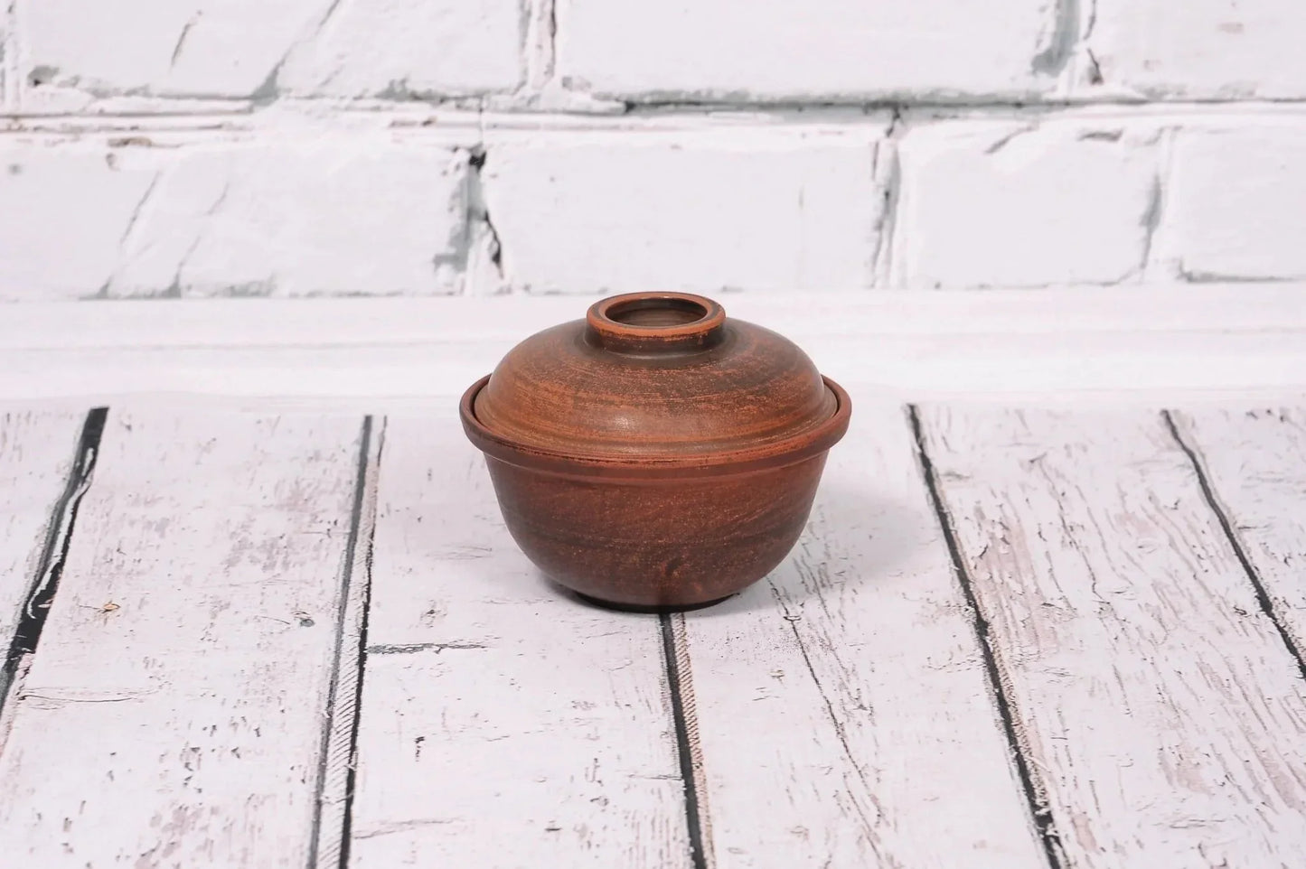 Handmade clay bowl with lid, rustic pottery bakeware on white wooden background