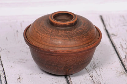 Handmade brown clay bowl with lid, rustic pottery bakeware on white wood background
