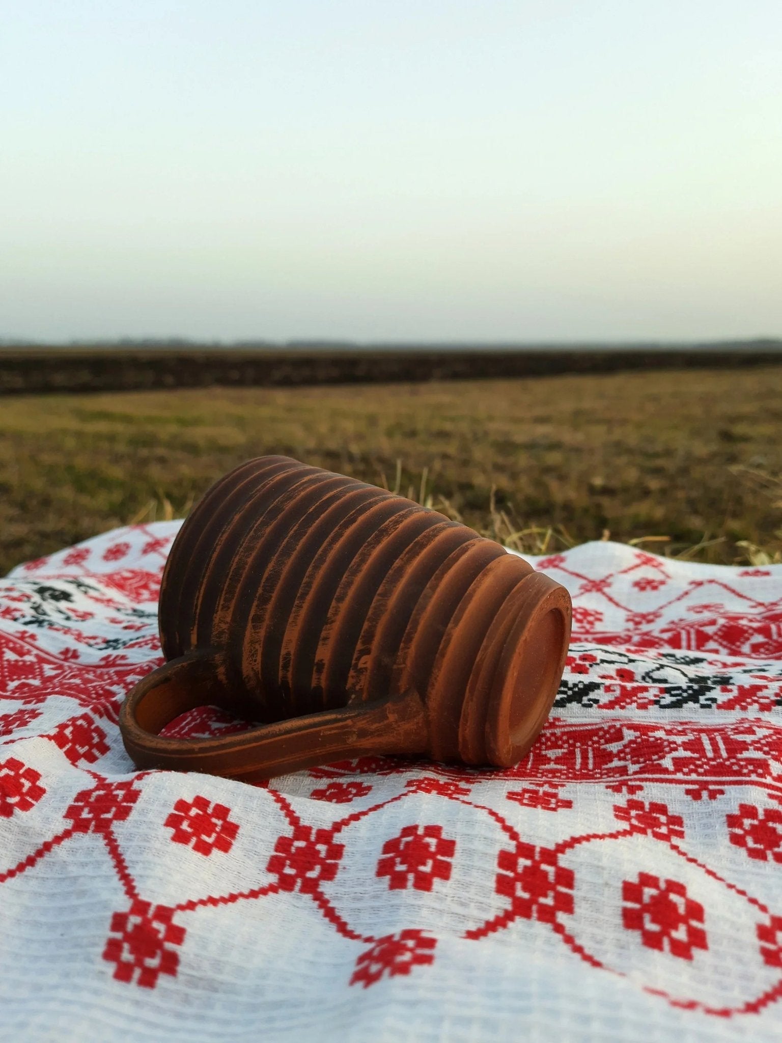 Handmade clay carved ceramic mug on embroidered cloth outdoors, artisan homeware