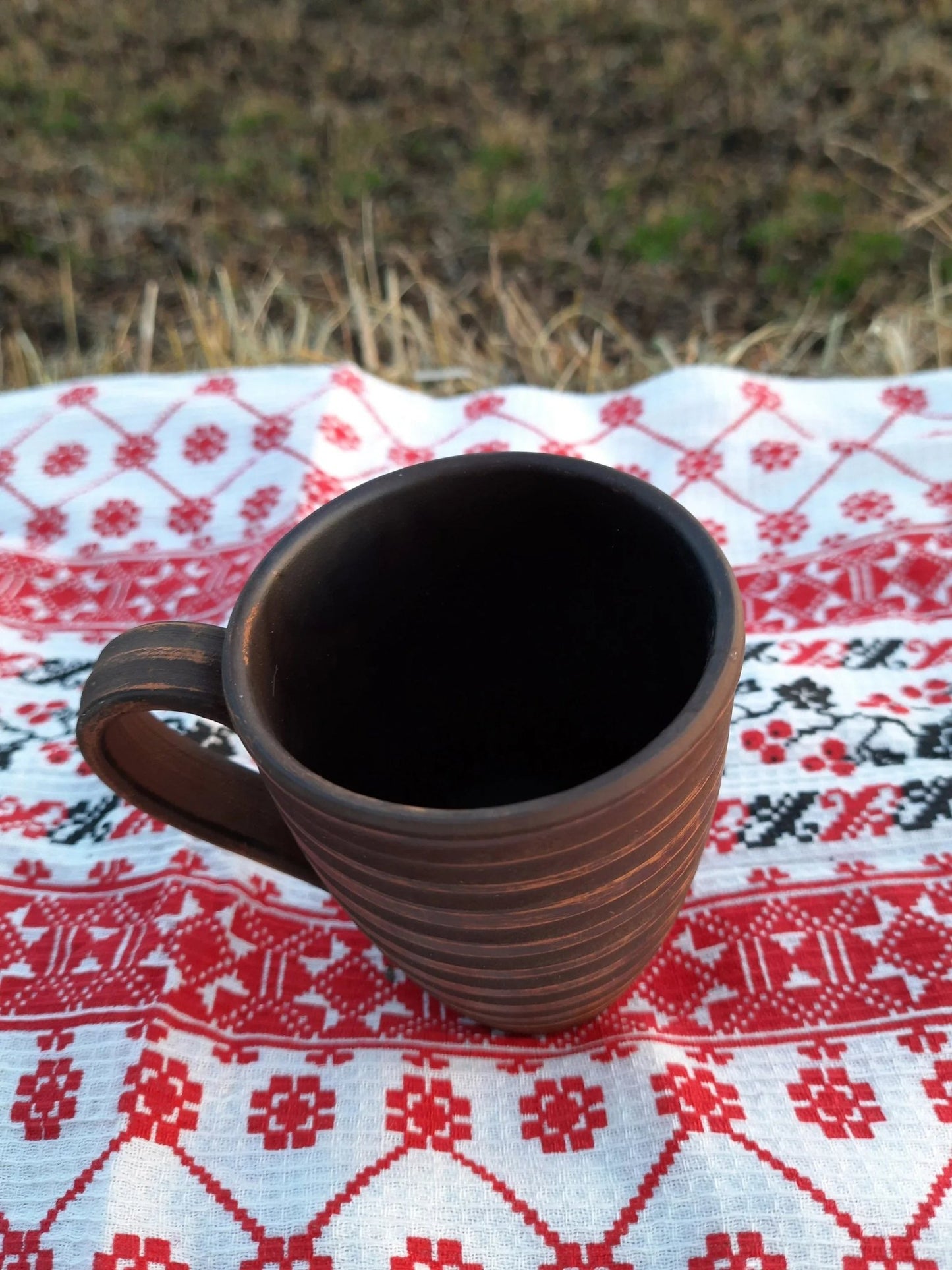 Handmade clay carved ceramic mug on embroidered red and white cloth outdoors