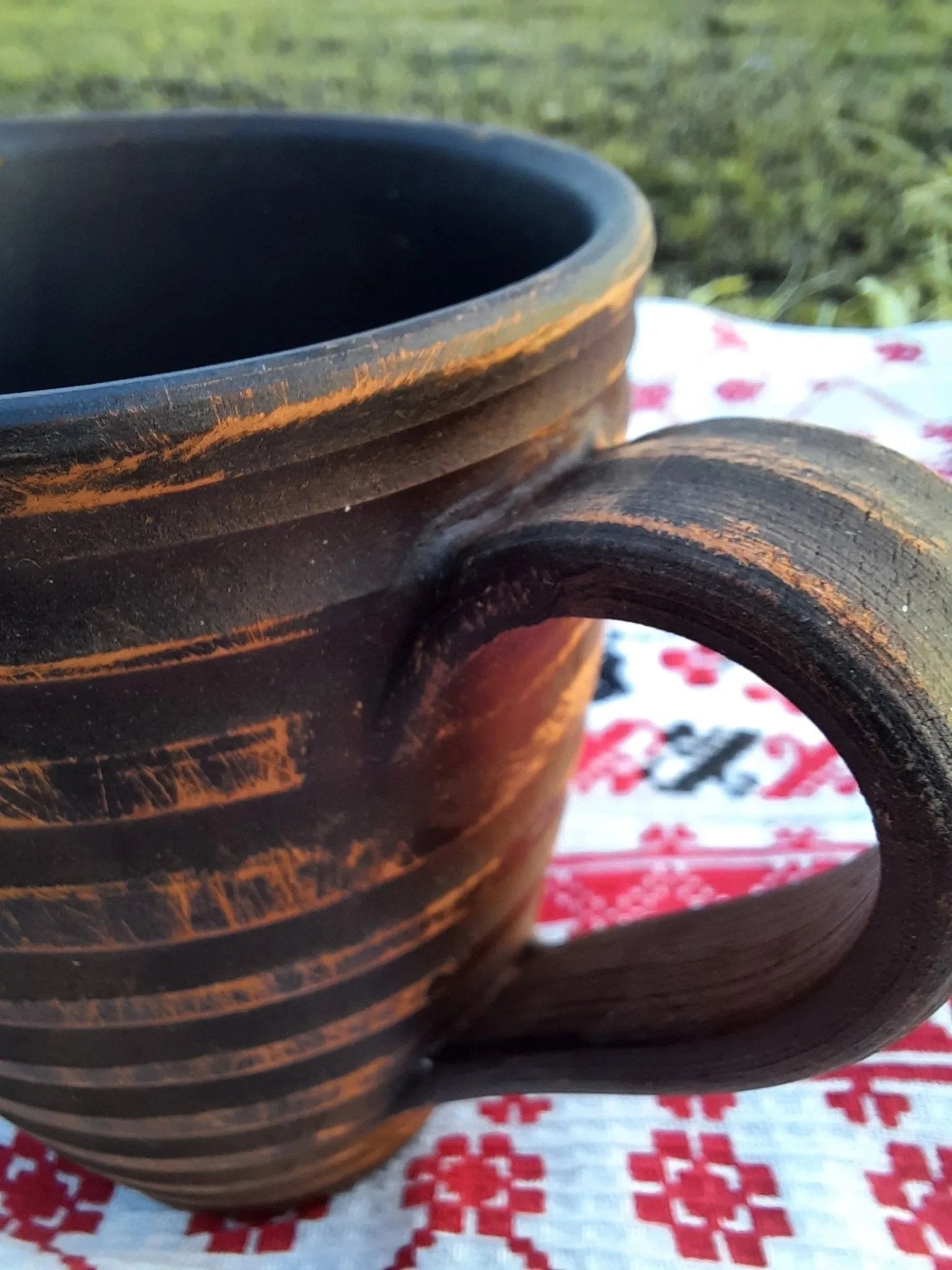 Handmade clay carved ceramic mug on patterned textile, artisan pottery homeware