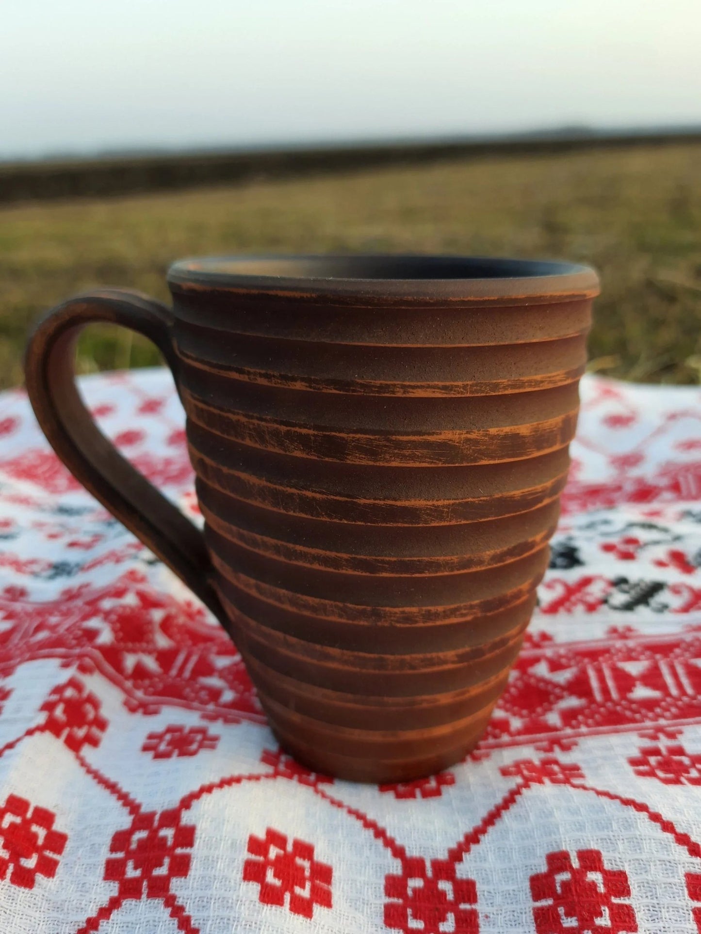Handmade clay carved ceramic cup on embroidered cloth, artisan pottery home decor