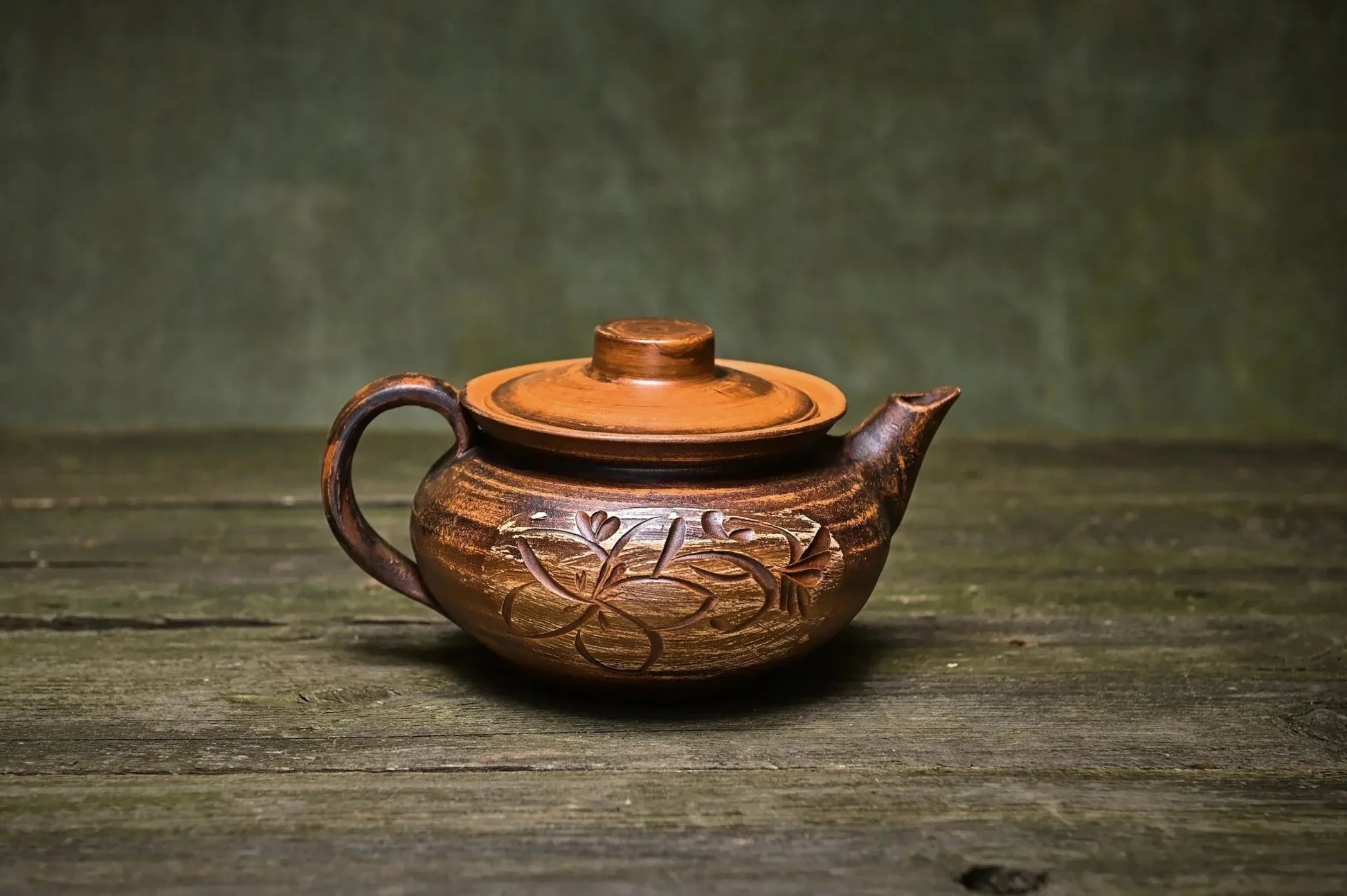 Handmade clay teapot with floral engraving on rustic wooden surface, artisan pottery decor