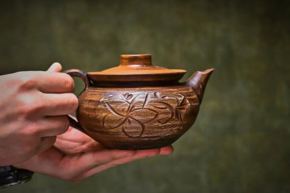 Hand holding handmade clay teapot with floral carvings, artisan home decor product