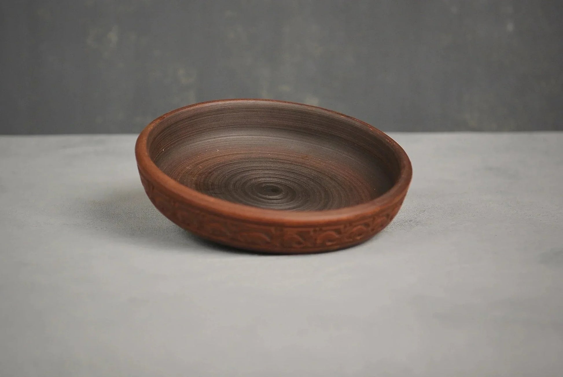 Handmade brown clay plate with engraved rim on a gray surface, artisan ceramic homeware