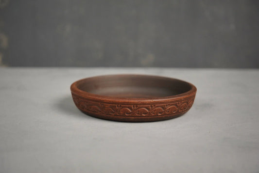 Handmade brown clay plate with engraved pattern, artisan ceramic homeware on gray background