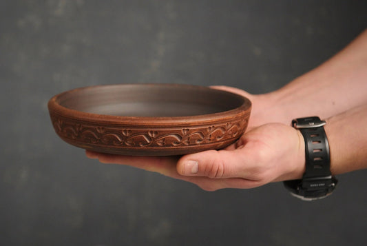 Hand holding a handmade brown clay plate with engraved floral patterns, clayproductsshop homeware