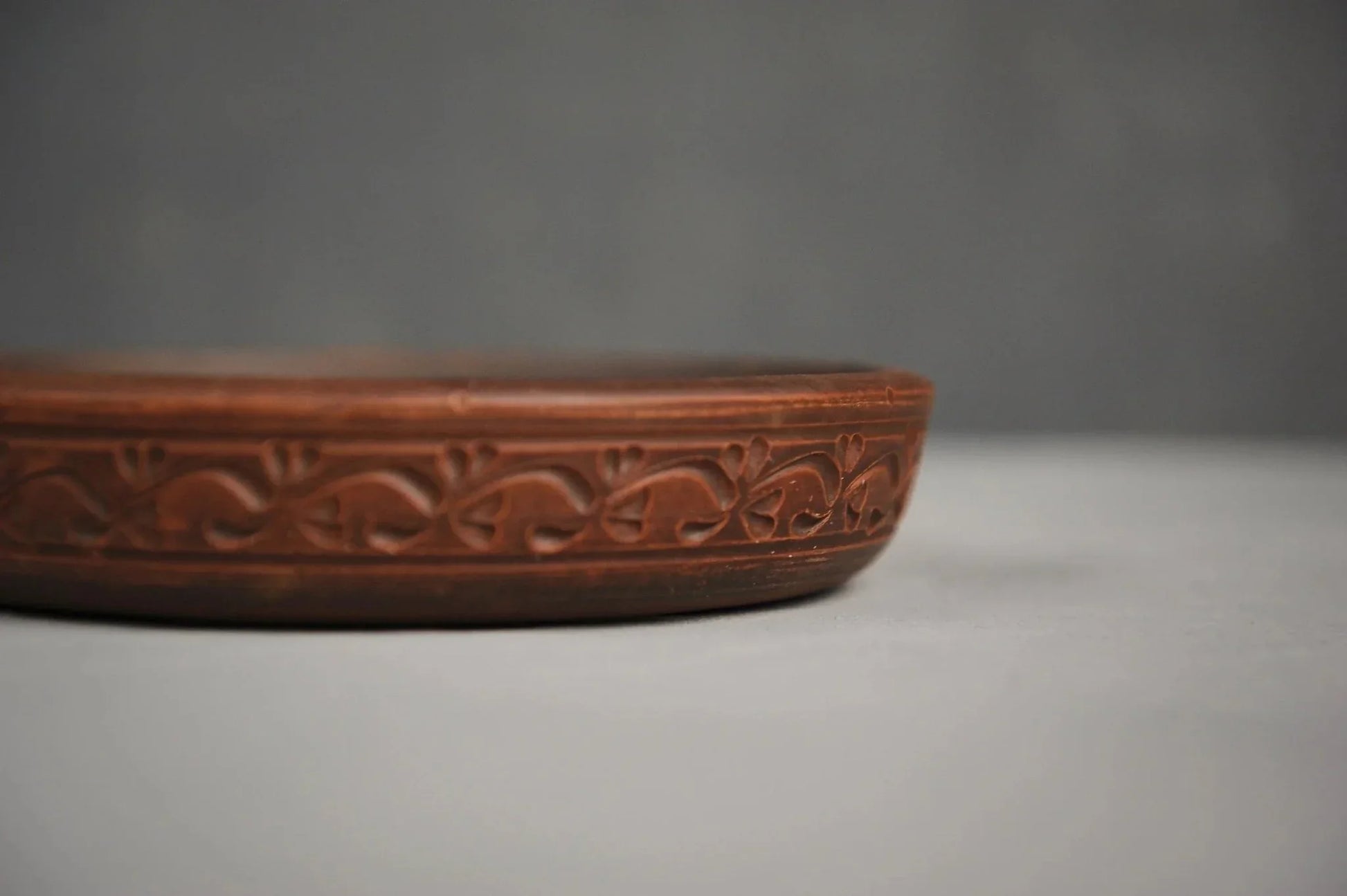 Handmade unglazed clay plate with intricate hand engraving, artisan brown round dish