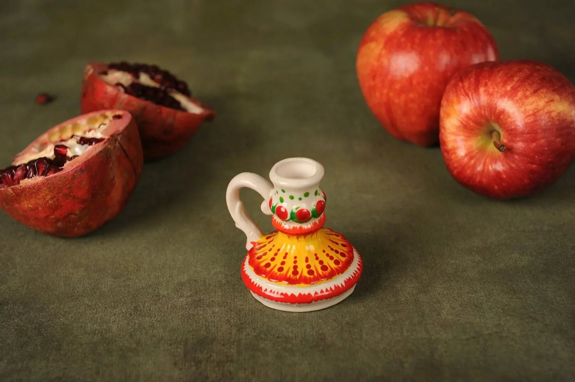Hand-painted ceramic candlestick holder with yellow and red patterns, surrounded by apples and pomegranate, artisan-crafted home decor from clayproductsshop.