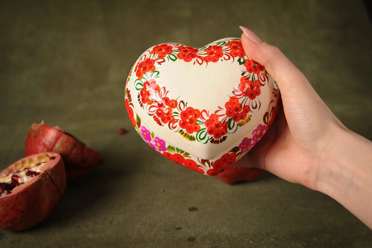Hand holding a heart-shaped hand-painted ceramic trinket box with red floral design