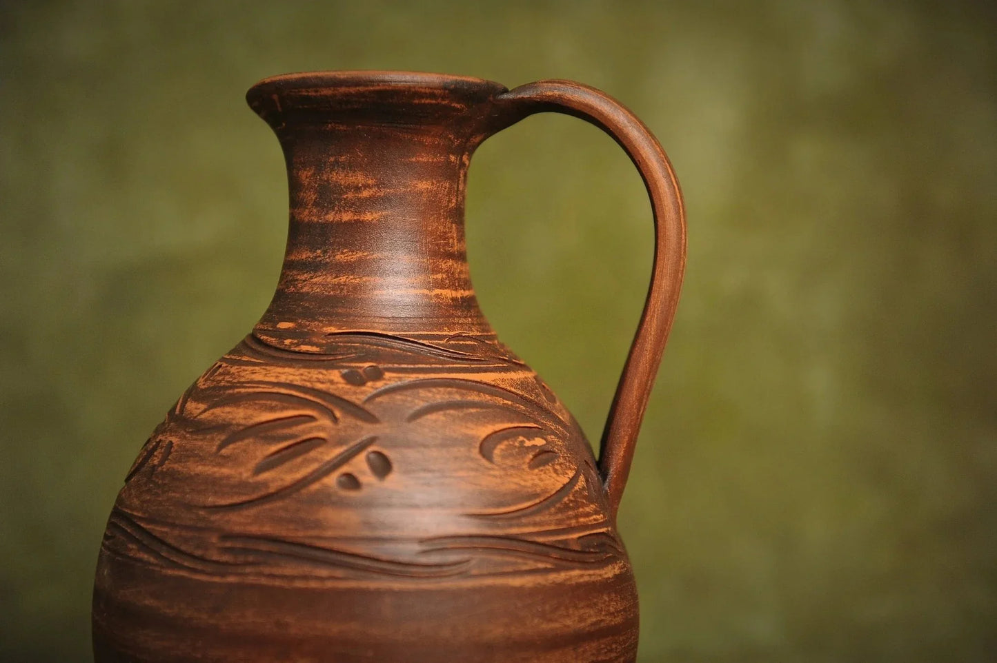 Handcrafted clay jug with carved patterns, artisan ceramic pitcher on neutral background