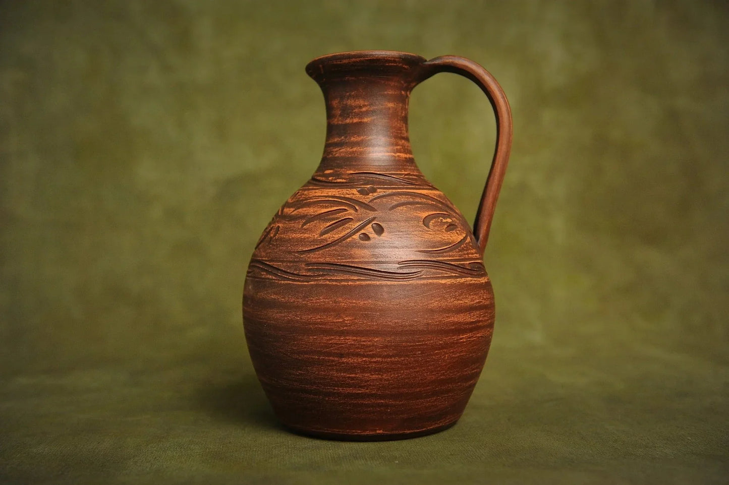Handcrafted brown ceramic clay jug with carved details on a plain green background