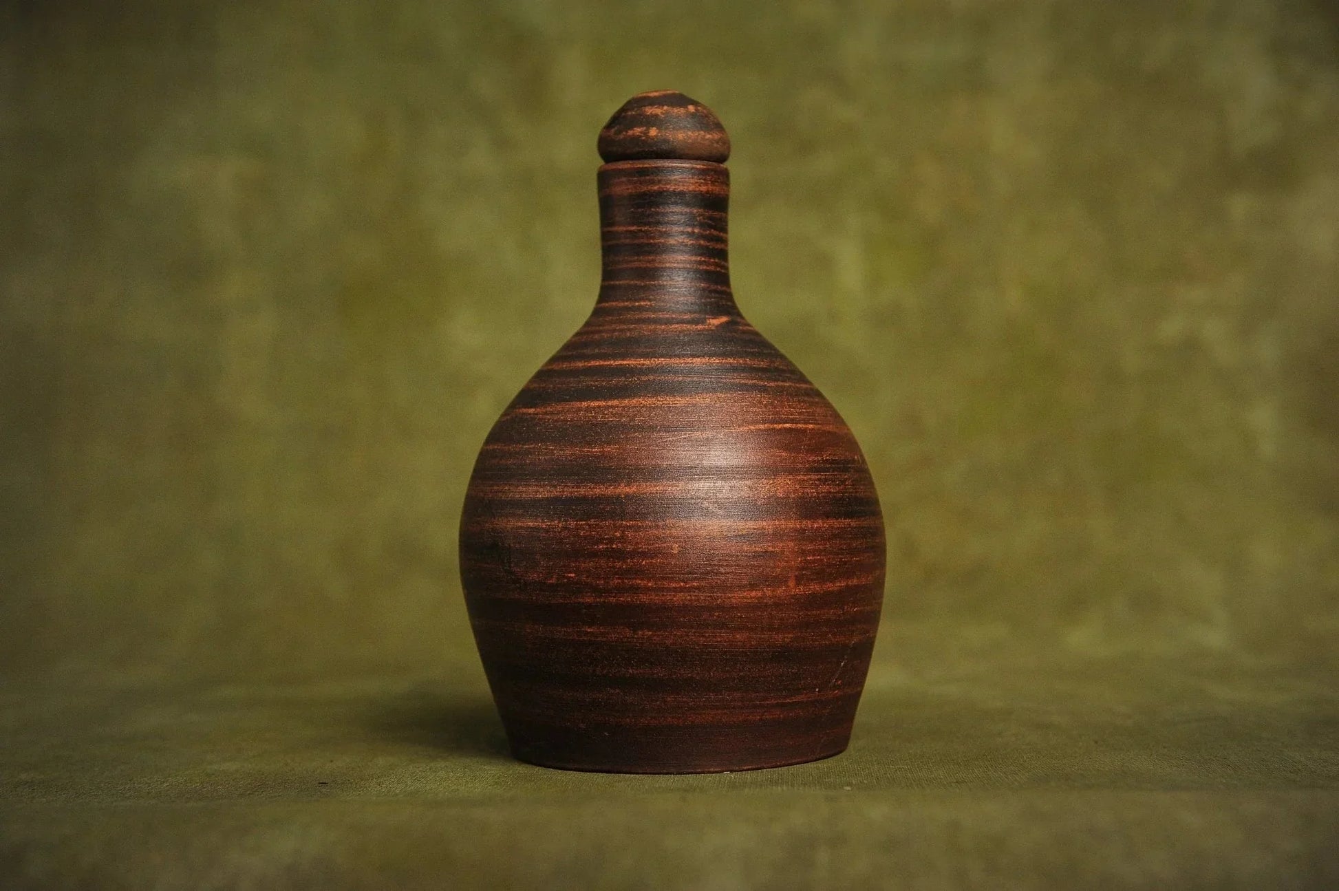 Handmade red clay jug vessel with lid on olive background, artisan home decor