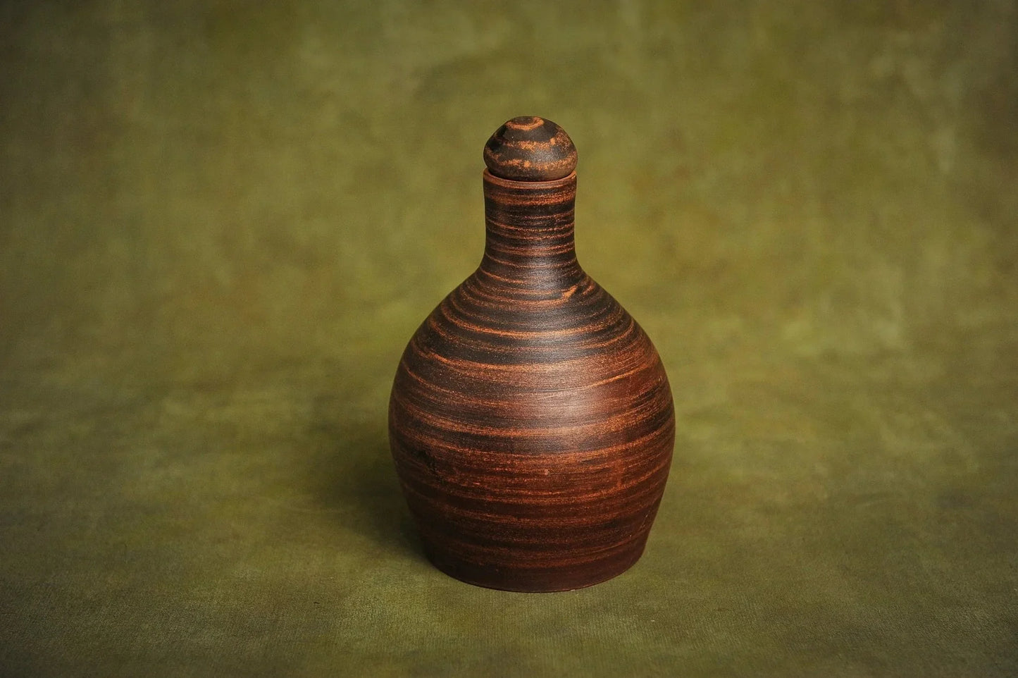 Handmade red clay bottle jug with lid on textured green background, artisan pottery homeware