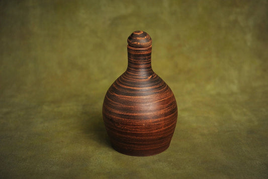 Handmade red clay bottle jug with lid on textured green background, artisan pottery homeware