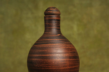 Handmade red clay jug with lid, artisan-crafted homeware on a green background