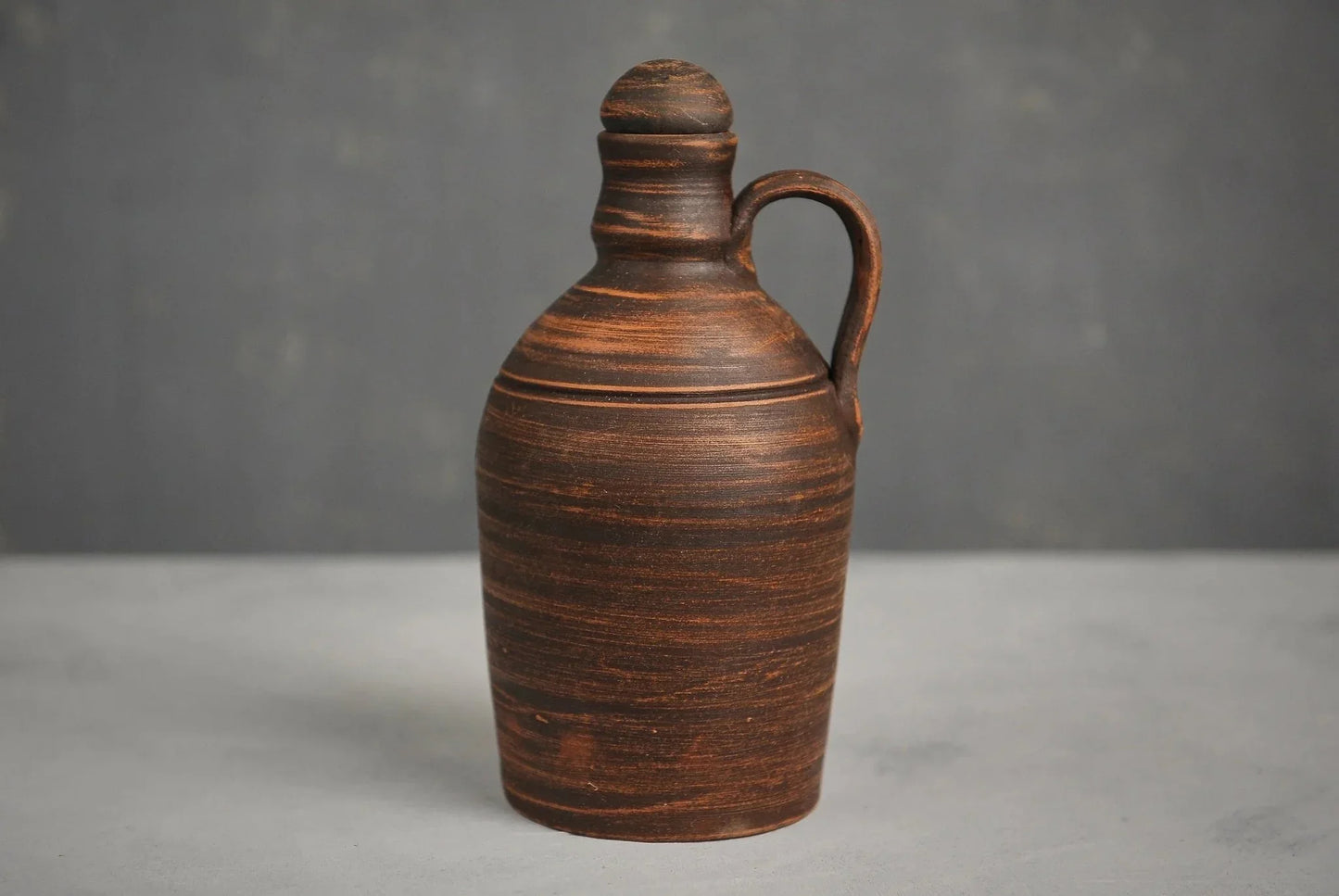 Handmade red clay bottle with handle and lid on a gray background, artisan homeware vessel
