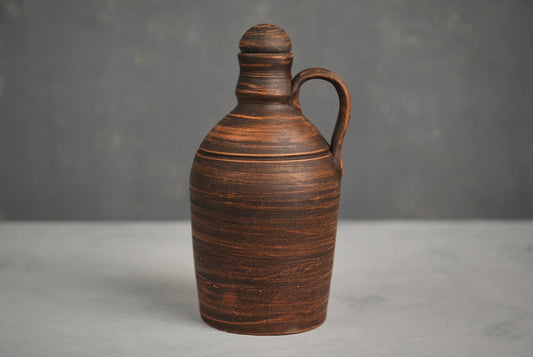 Handmade red clay bottle with handle and lid on a gray background, artisan homeware vessel