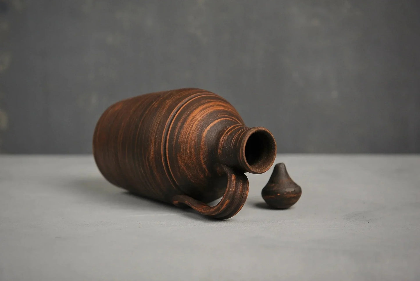 Handmade red clay jug with handle and lid, rustic artisan pitcher on gray surface