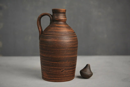 Handmade red clay jug with handle and lid on grey background, artisan home decor vessel