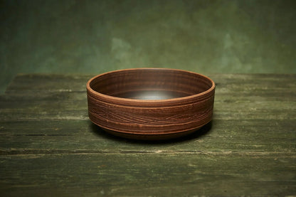 Handmade ceramic clay bowl with carved design on rustic wood surface