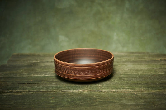 Handmade ceramic clay bowl with textured pattern on rustic wooden surface