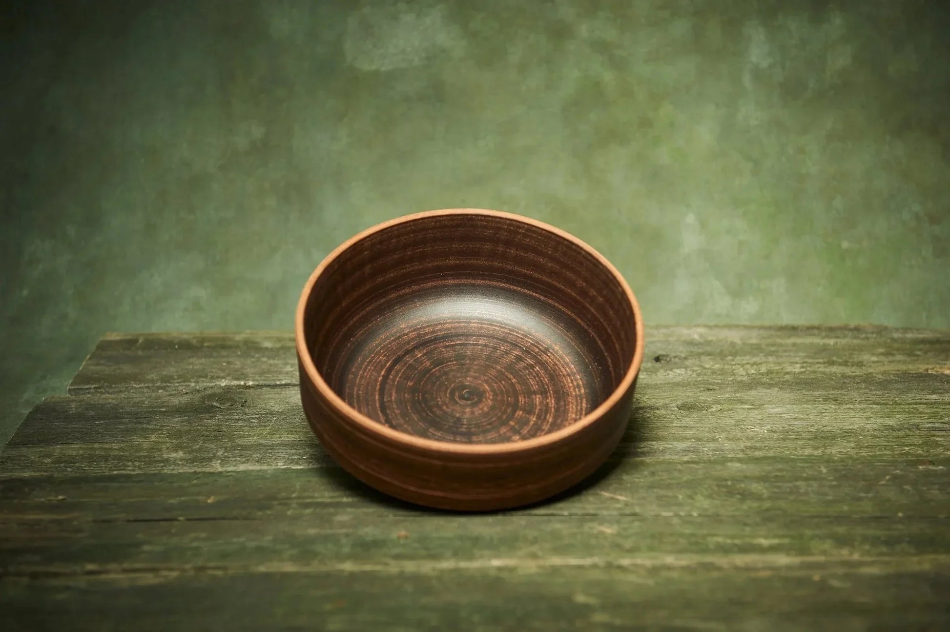 Handmade ceramic clay bowl with subtle brown spiral pattern on rustic wooden table