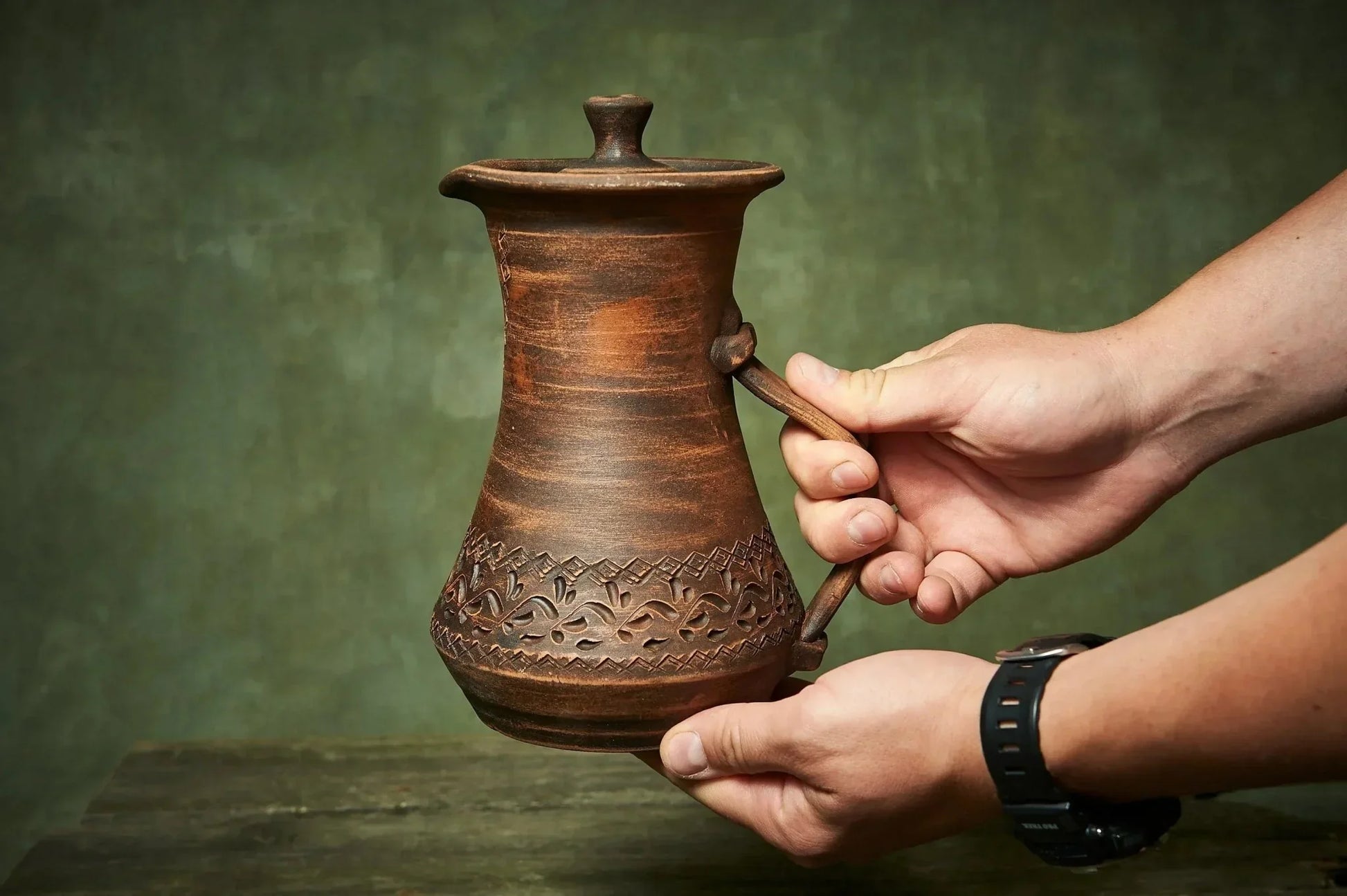Hand holding handmade ceramic clay pitcher with lid, rustic farmhouse pottery jug
