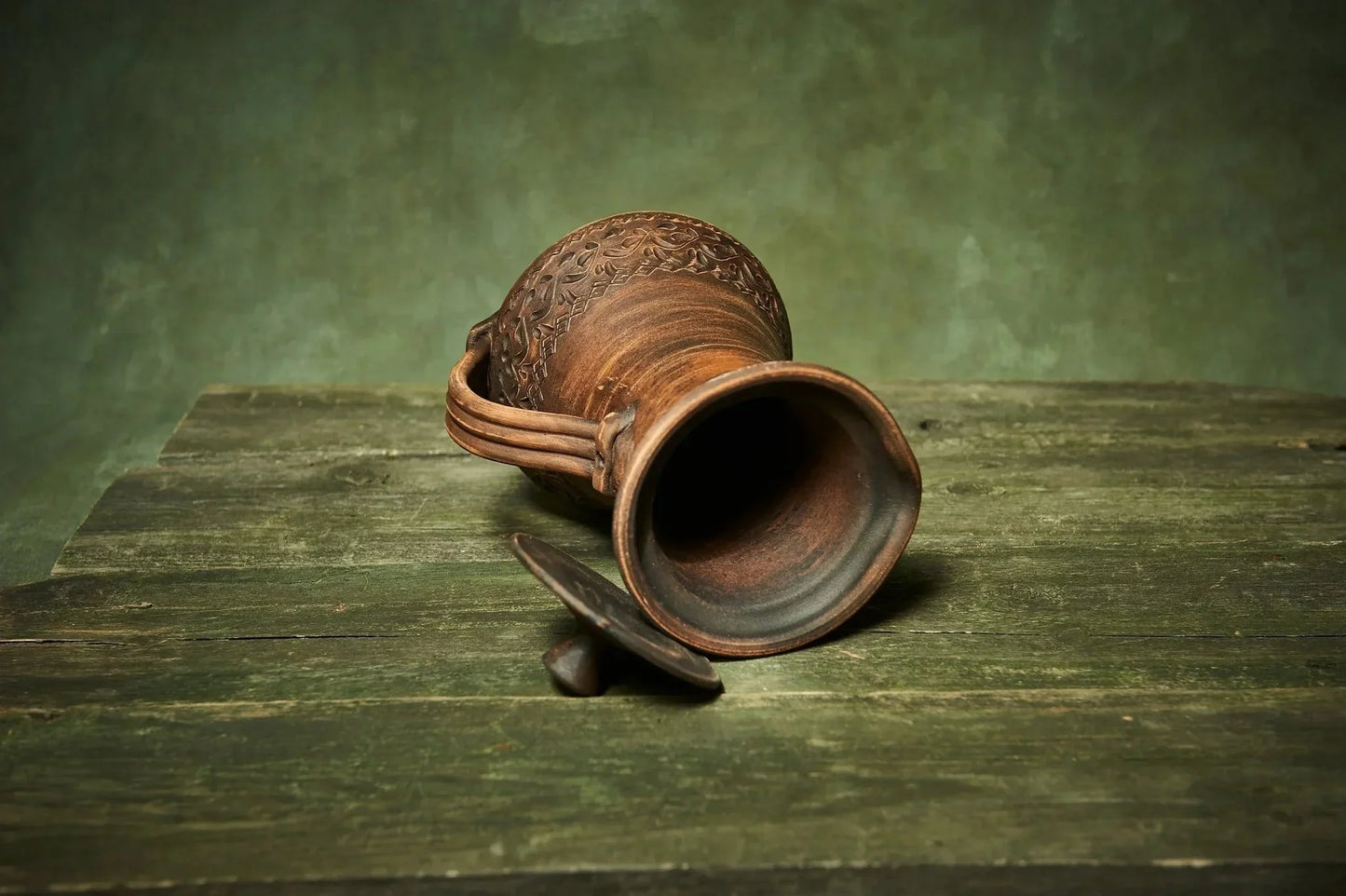 Handmade ceramic pitcher with lid, rustic clay homeware on wooden surface