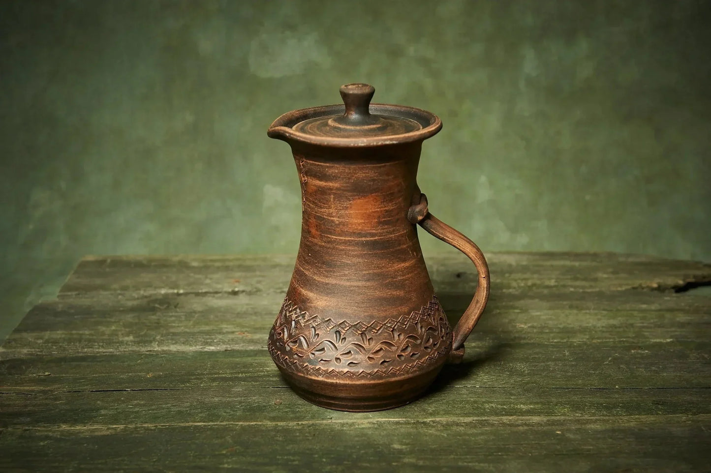 Handmade clay pitcher with lid and handle, rustic ceramic jug on wooden surface, farmhouse decor