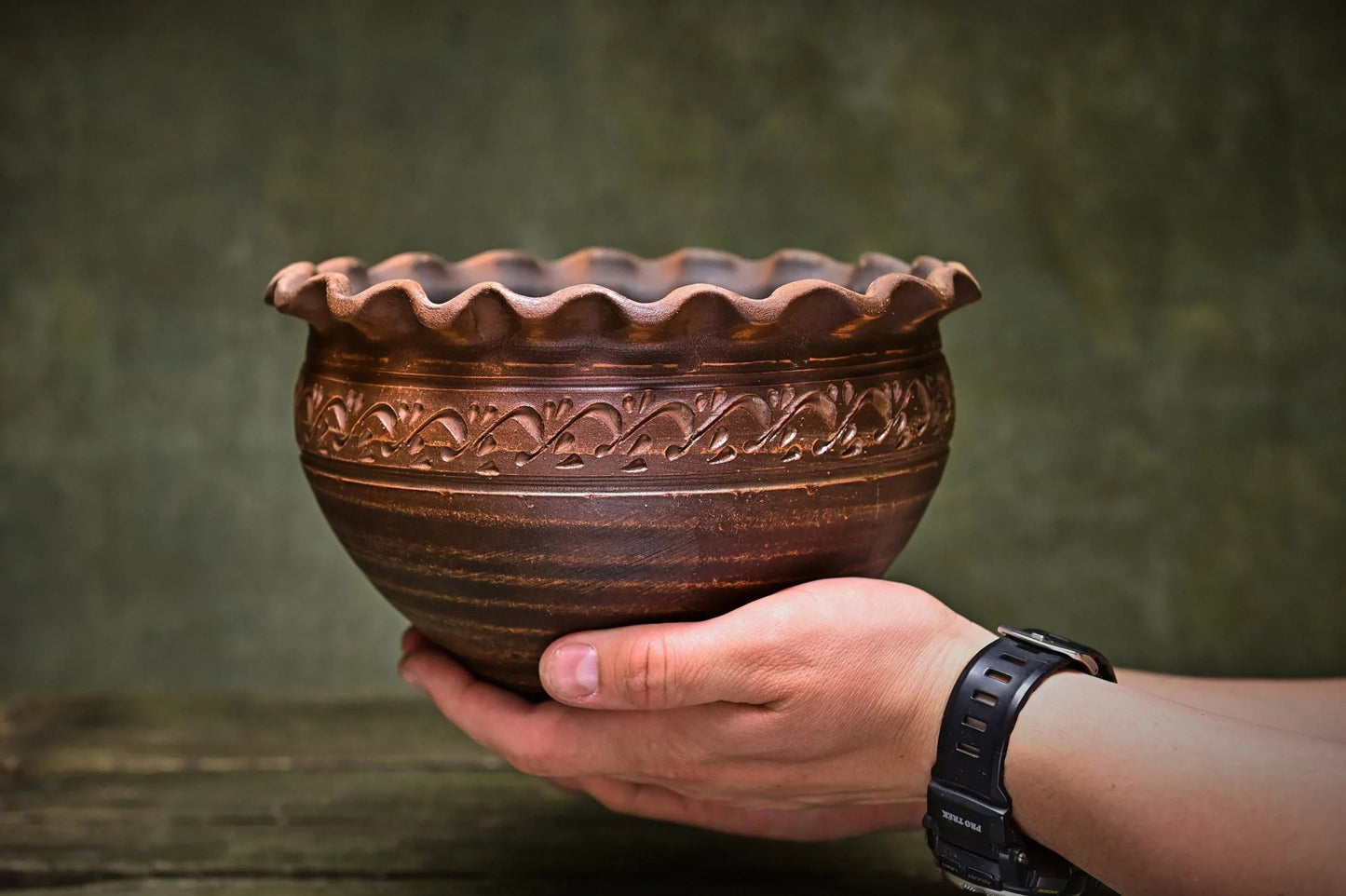 Hand holding a handmade Ukrainian ceramic clay bowl with ornate rim and decorative pattern.