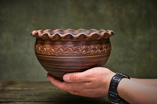 Hand holding a handmade Ukrainian ceramic clay bowl with ornate rim and decorative pattern.