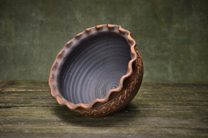 Handmade ceramic clay bowl with wavy rim and embossed detailing on rustic wood