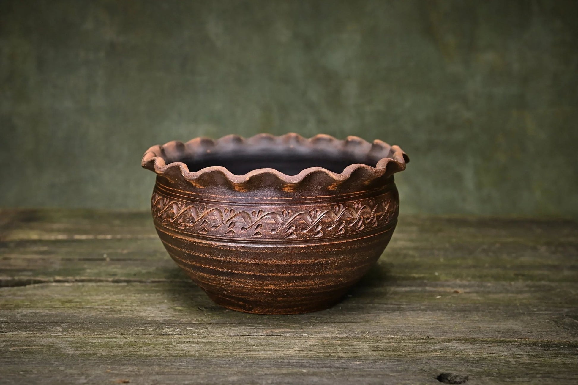 Handmade ceramic clay bowl with wavy rim and carved pattern, rustic pottery on wood surface