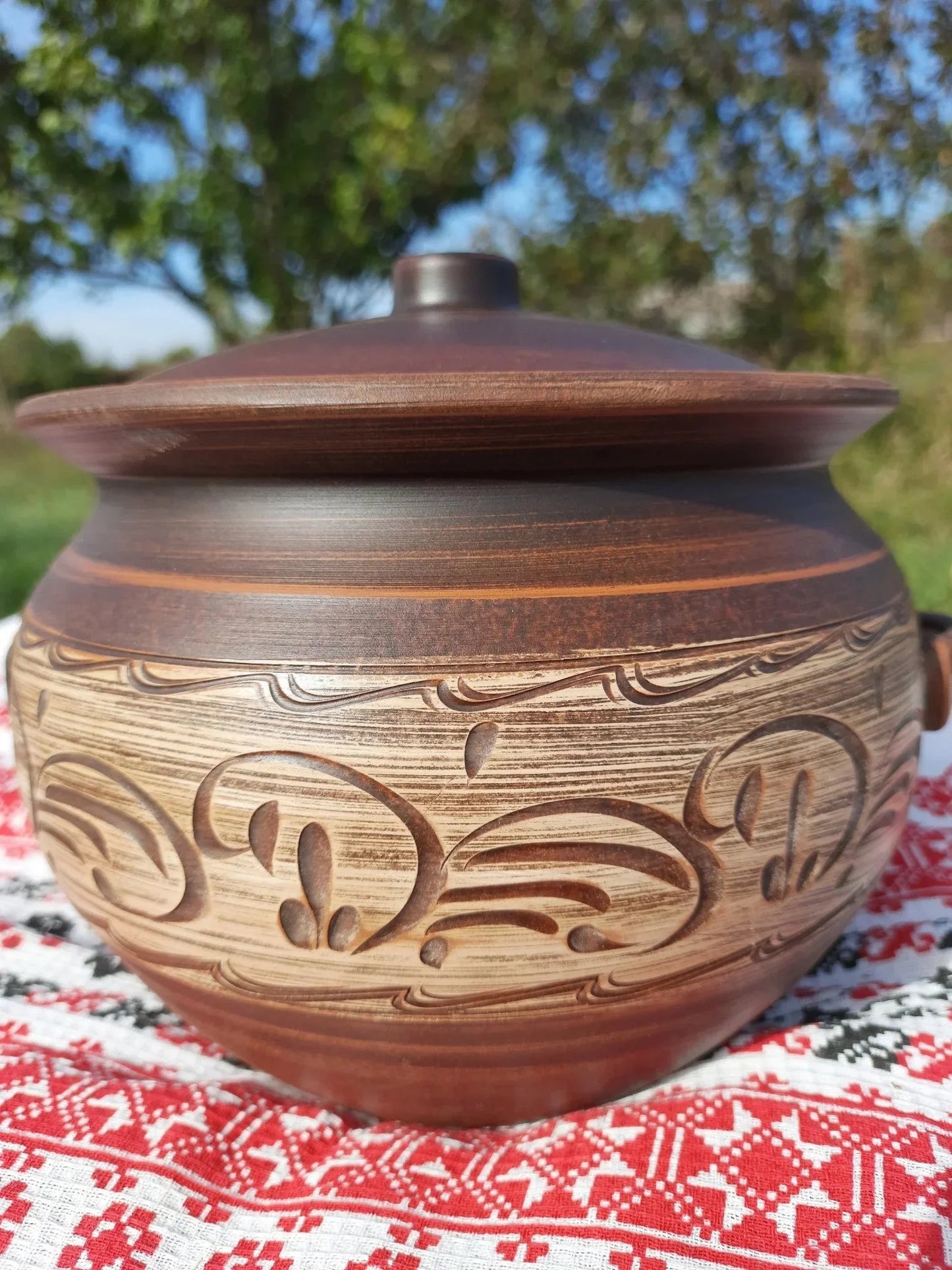 Handmade red clay ceramic pot with lid and decorative carvings on traditional cloth