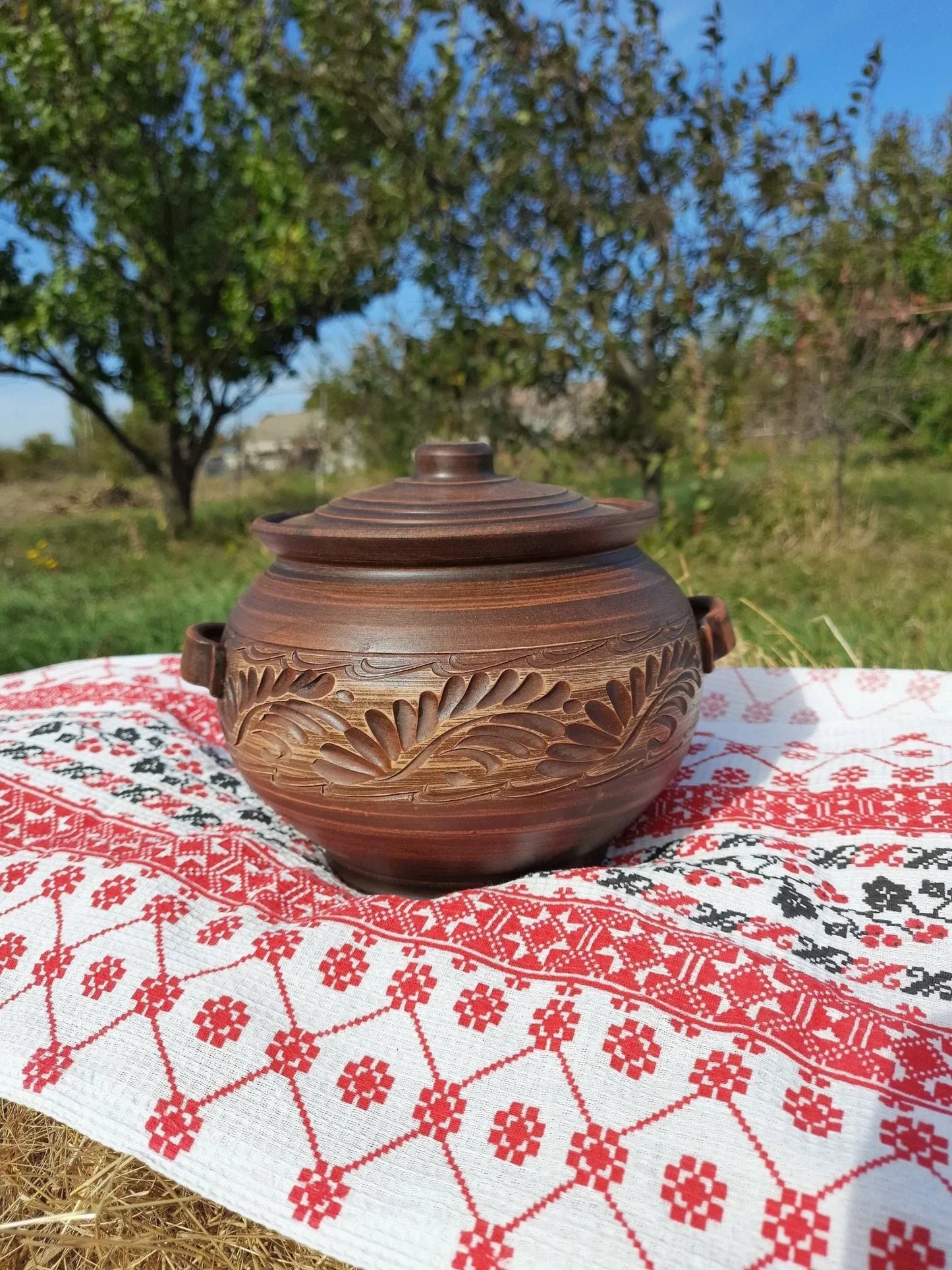 Handmade ceramic pot with lid and handles on embroidered cloth, artisan clay homeware outdoors