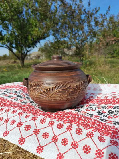 Handmade ceramic pot with lid and handles on embroidered cloth, artisan clay homeware outdoors