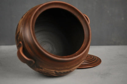 Handmade ceramic pot with handles and lid, artisanal clay cookware on grey background