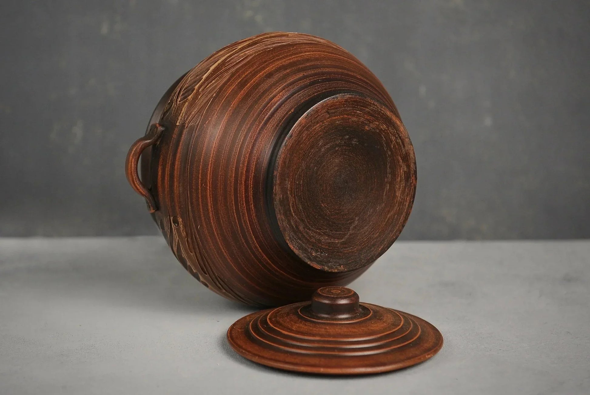 Handmade ceramic pot with handles and lid, artisanal brown clay cookware on gray background
