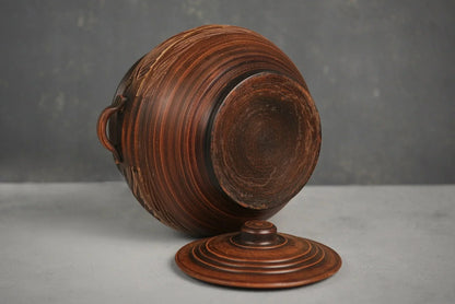 Handmade ceramic pot with handles and lid, artisanal brown clay cookware on gray background