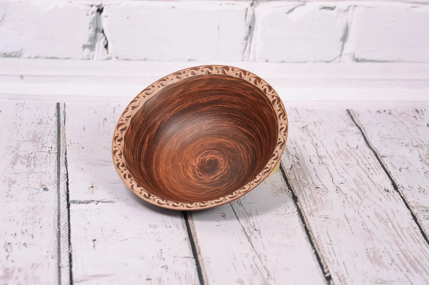 Handmade clay bowl with decorative rim, rustic pottery for soup, on white wooden background
