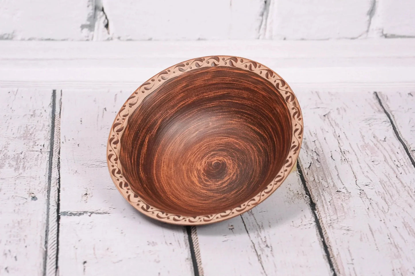 Handmade clay bowl with decorative rim, rustic ceramic pottery on white wooden surface