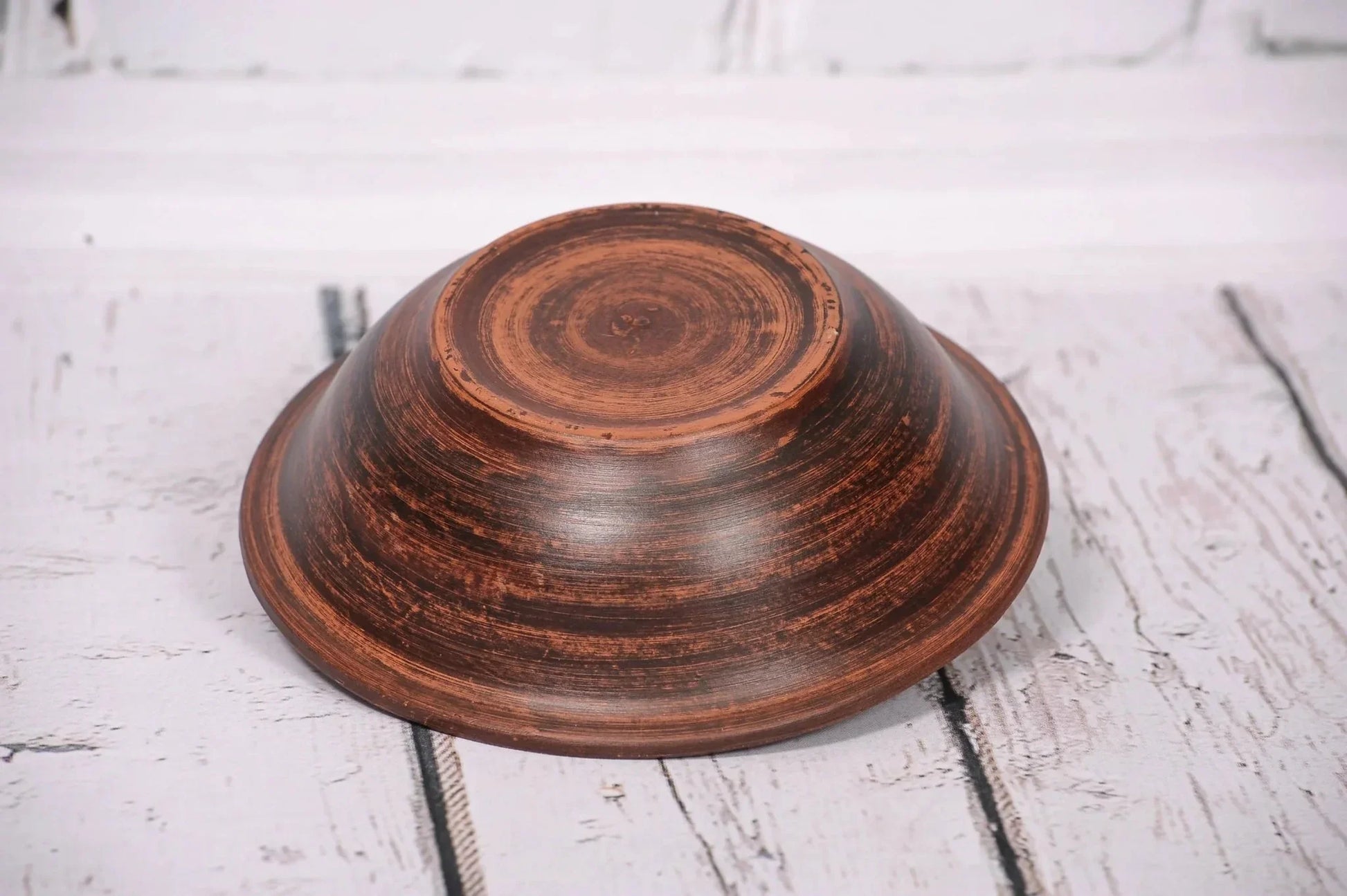 Handmade clay bowl upside down on rustic white wood, artisan handcrafted pottery product